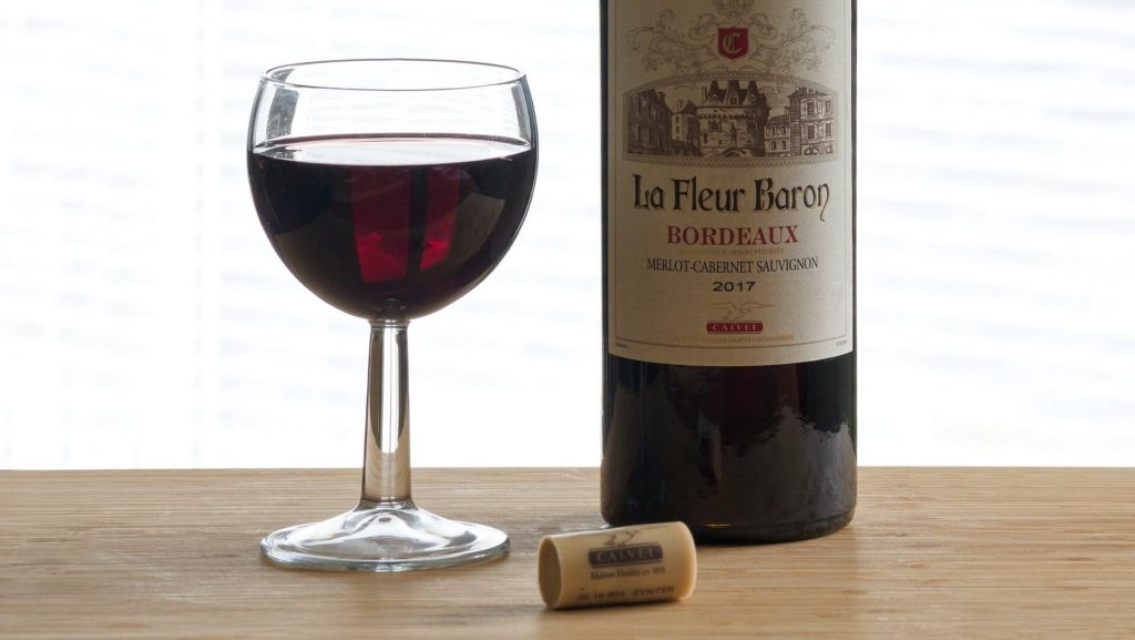 Una copa llena de vino de mezcla de Burdeos junto a una elegante botella de vino