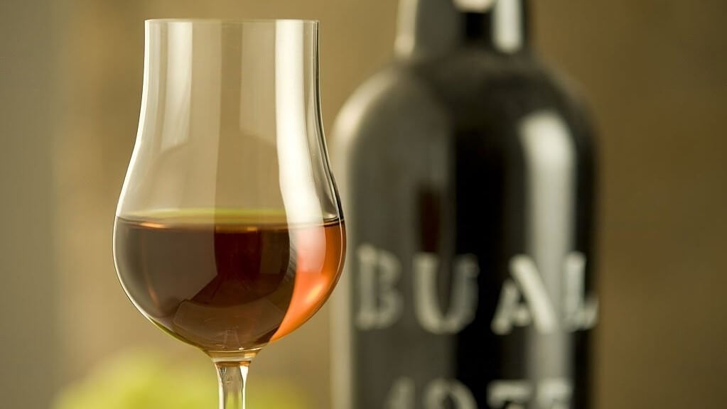 Una copa de rico vino de Madeira junto a una apetecible botella del mismo.